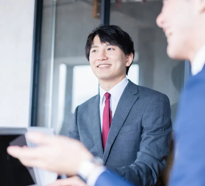 オフィスで、フレームに映っていない人物とコミュニケーションしている笑顔の若いビジネスマン